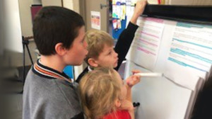 Three students in a classroom problem solving on a whiteboard together.