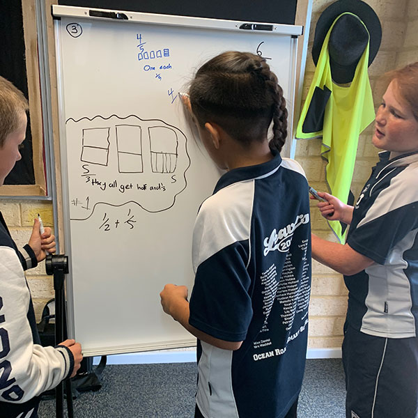 Three primary school children drawing fractions on a whiteboard.