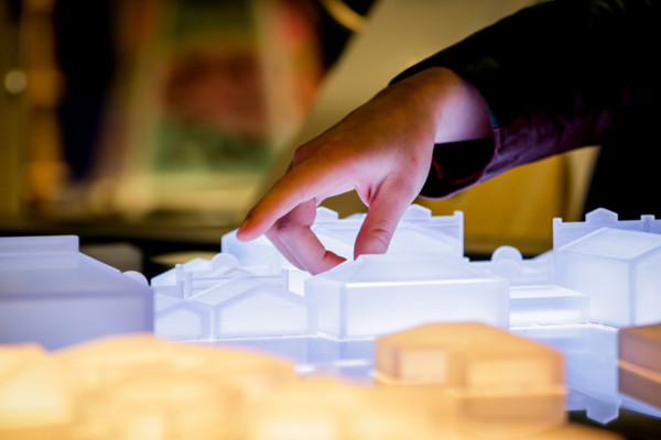 Hands gesturing to 3D printed buildings illuminated by LED lights