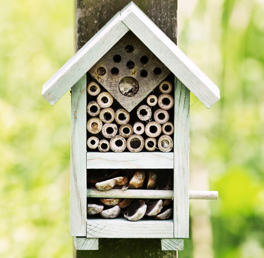 Close up of a small insect hotel with a triangle shaped roof, attached to a wooden post