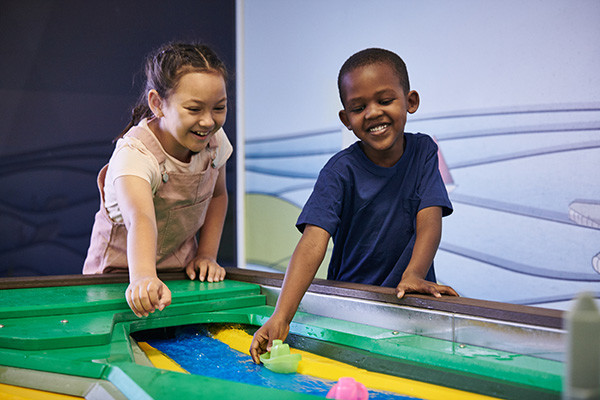 Two young children playing in Discoverland in a water exhibit with rubber ducks.