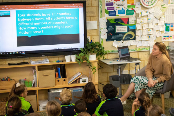 A teacher showing a primary classroom a powerpoint presentation.