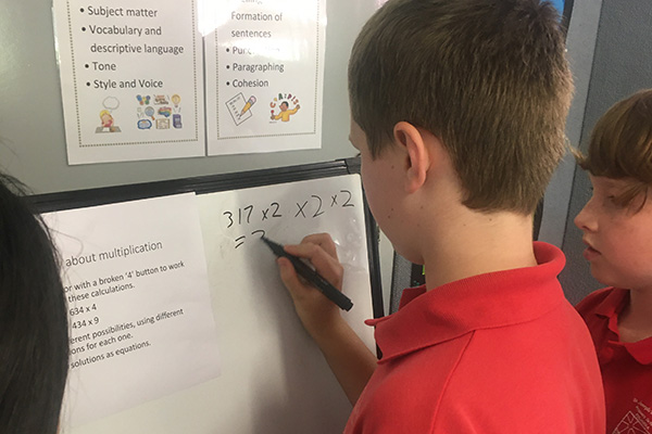 A young male primary student writing maths equations on a whiteboard.