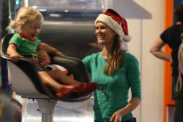 A woman wearing a christmas hat spinning her child in a chair gleefully.