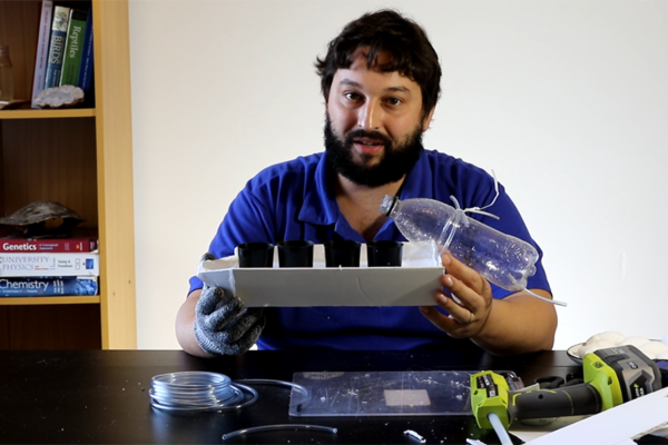 Scitech presenter holding boat made from household items including plastic and can holders.