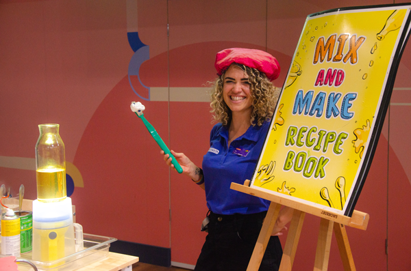 Woman standing next to an easel that says 'Mix and Make Recipe book'